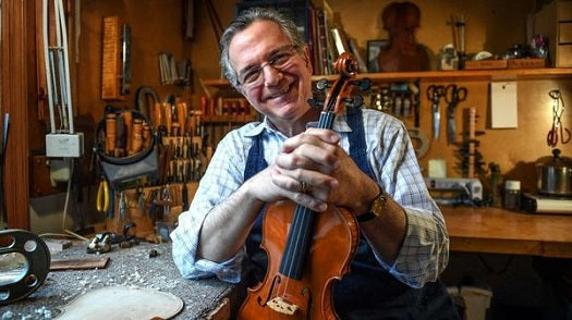 Master Violin Maker Charles Rufino posing with violin in his shop